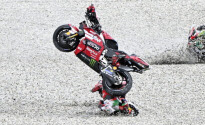 MotoGP rider crashes while performing a stunt on a red Ducati bike on a gravel track.