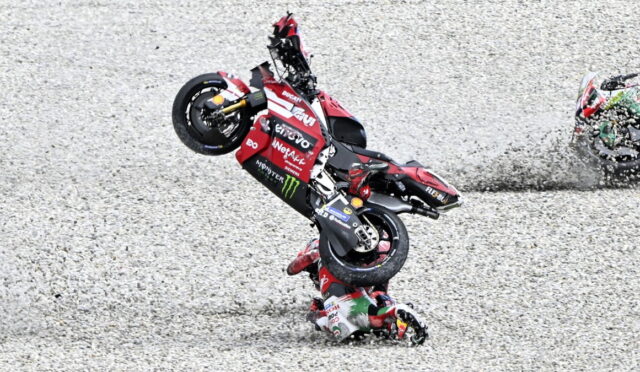 MotoGP rider crashes while performing a stunt on a red Ducati bike on a gravel track.