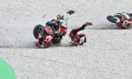 Racing motorcyclist crashes on gravel track as another rider slides nearby in a red suit and bike nearby