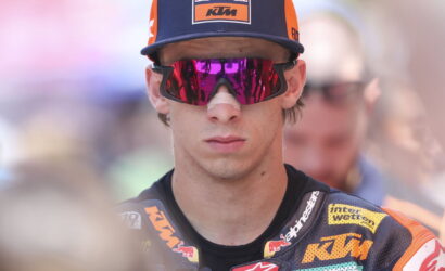 Moto rider wearing a Red Bull KTM cap and mirrored pink sunglasses, in a racing suit with sponsor logos.