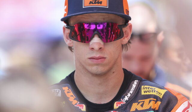 Moto rider wearing a Red Bull KTM cap and mirrored pink sunglasses, in a racing suit with sponsor logos.