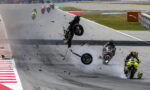 Motorcycle crash on track: a rider and bike are airborne as debris and smoke scatter across the circuit.
