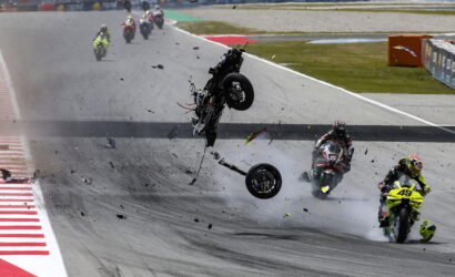 Motorcycle crash on track: a rider and bike are airborne as debris and smoke scatter across the circuit.