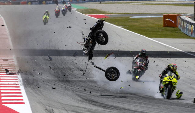 Motorcycle crash on track: a rider and bike are airborne as debris and smoke scatter across the circuit.