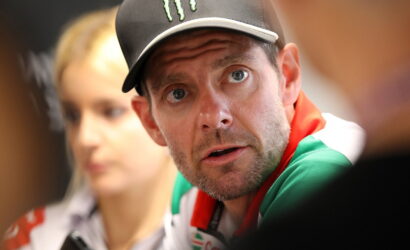 Man wearing a black cap with a Monster logo, looking surprised with wide eyes and a blurred background person behind him.