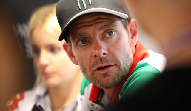 Man wearing a black cap with a Monster logo, looking surprised with wide eyes and a blurred background person behind him.