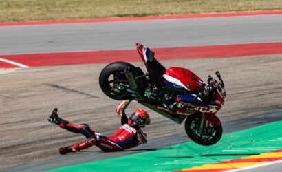 Motorcycle racer in red gear crashes on the track, sliding across the asphalt as the red-green bike tips upward nearby.