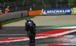 Rear view of a Yamaha racing bike and rider on a track, leaning into a turn with red and white painted curbs and Michelin banners in the background.