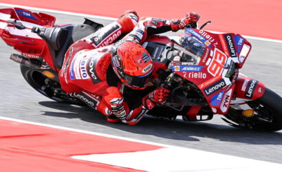 Red MotoGP rider in red leathers leaning into a corner on a sponsor-covered race bike.