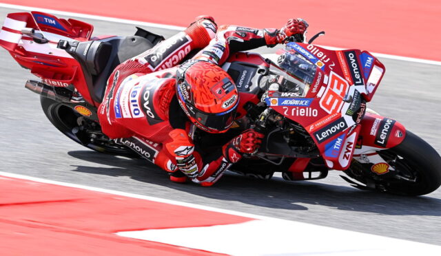 Red MotoGP rider in red leathers leaning into a corner on a sponsor-covered race bike.