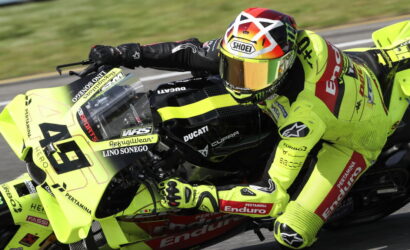 Motorsport rider on a neon yellow Ducati race bike leaning into a turn at speed, wearing matching neon leathers and helmet.