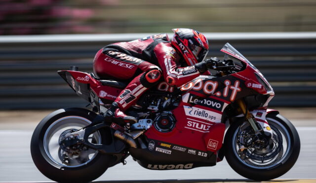 Rider in red racing suit on a red Ducati motorcycle speeding on a race track with sponsor logos visible