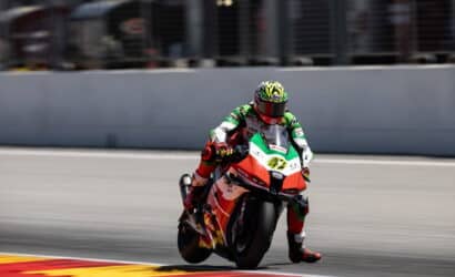 Moto racer in green-white-red suit leaning into a turn on a race bike with red accents on a track.