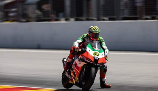 Moto racer in green-white-red suit leaning into a turn on a race bike with red accents on a track.