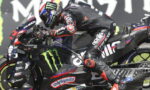 Moto racer leaning into a sharp turn on a black Monster Energy Yamaha bike adorned with sponsor decals in a high-speed track setting