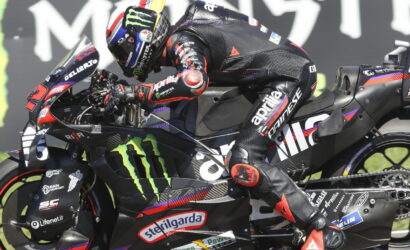 Moto racer leaning into a sharp turn on a black Monster Energy Yamaha bike adorned with sponsor decals in a high-speed track setting