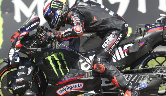 Moto racer leaning into a sharp turn on a black Monster Energy Yamaha bike adorned with sponsor decals in a high-speed track setting