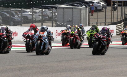 Group of motorcycle racers in a tight pack leaning into a turn on a race track