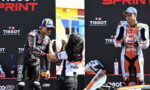 Two motorcyclists on a podium as a staffer hands a medal to the left rider, with sponsor banners behind (TISSOT).