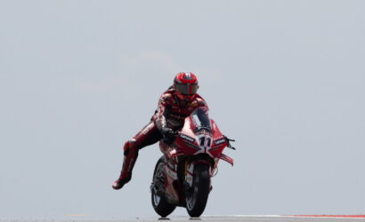 Professional motorcycle racer in a red suit and helmet riding a red race bike with number 11 on a track, leaning into a turn