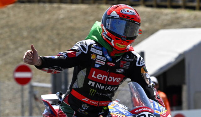 Motorcycle racer in a red Suomy helmet and Lenovo racing suit giving a thumbs-up on the track.