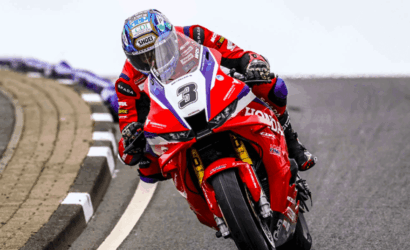 Motorcycle racer in a red racing suit leaning into a curve on a paved track, bike number 3.