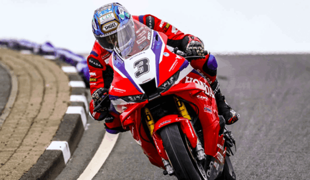 Motorcycle racer in a red racing suit leaning into a curve on a paved track, bike number 3.
