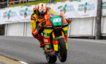 Rider in a bright, multicolor racing suit and helmet leaning into a corner on a race track with the number 60 on the bike.