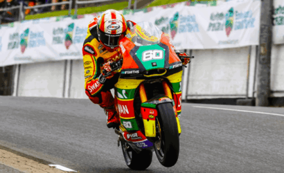Rider in a bright, multicolor racing suit and helmet leaning into a corner on a race track with the number 60 on the bike.