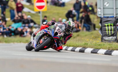 Motorcycle racer leaning into a sharp turn on a road race, bike number 10, spectators in the background.
