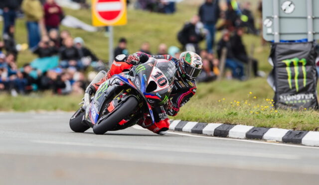 Moto motorcycle racer in a tight lean on a curving road, number 10 bike, spectators in the background watching the race.