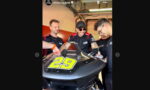 Team members in matching black and red shirts work on a race bike with the number 29 in a garage.