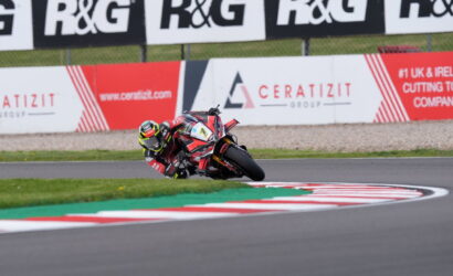 Motorcycle racer leans into a tight left-hand turn on a race track, red‑white curbs visible ahead.