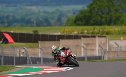 Motorcycle racer in red and green leans into a sharp corner on a race track.
