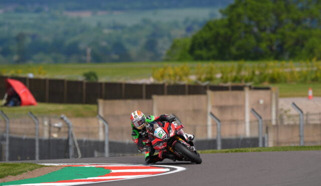 Motorcycle racer in red and green leans into a sharp corner on a race track.