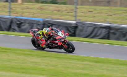 Motorcycle racer in red and black leans into a turn on a race track, yellow helmet, red Ducati bike.