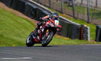 Motorcyclist in red, white, and black racing gear leans into a sharp turn on a race track.