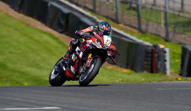 Motorcyclist in red, white, and black racing gear leans into a sharp turn on a race track.