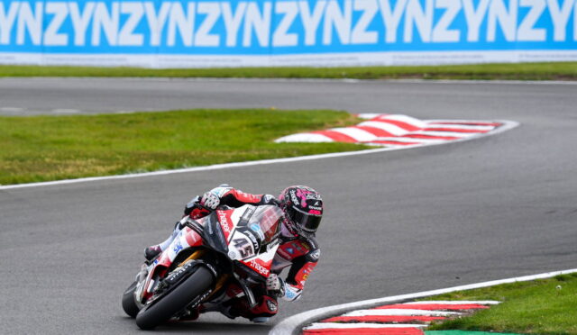 Motorcycle racer in red and white gear leaning into a sharp turn on a race track; bike number 41 with sponsor logos, blue ad banners in the background.