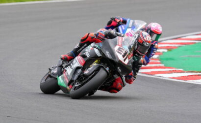 Three motorcycle racers lean into a sharp turn on a race track, close together in a tight corner.