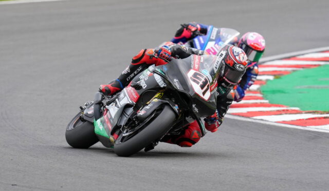 Three motorcycle racers lean into a sharp turn on a race track, close together in a tight corner.