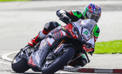 Motorcycle racer in colorful gear leaning into a sharp turn on a track, body tucked close to the bike for speed.