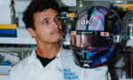 Male researcher in a white lab coat gazes at a colorful, logo-covered racing helmet in a lab setting.