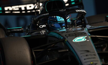 Mercedes-AMG Petronas Formula 1 car in teal and black, driver visible in the cockpit with blue helmet, close-up on front and halo protection.