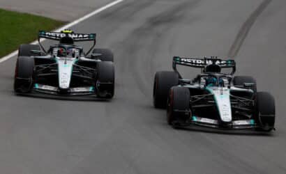 Two Mercedes Formula 1 cars race side by side on a gray track, front wings low and tires gripping the asphalt, Petronas branding on rear wings.
