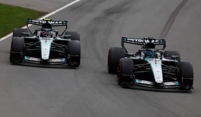 Two Mercedes Formula 1 cars race side by side on a gray track, front wings low and tires gripping the asphalt, Petronas branding on rear wings.
