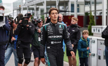Formula 1 driver in a Petronas Mercedes suit walks past a crowd of photographers at a race event.