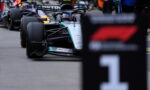 Mercedes Formula One car in the pit area, driver in helmet, with team branding Petronas visible on the car's nose and sidepod.