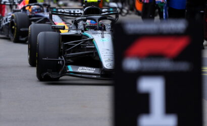 Mercedes Formula One car in the pit area, driver in helmet, with team branding Petronas visible on the car's nose and sidepod.