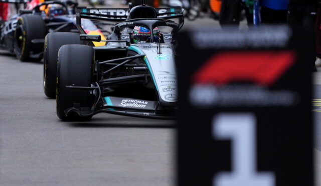 Mercedes Formula One car in the pit area, driver in helmet, with team branding Petronas visible on the car's nose and sidepod.
